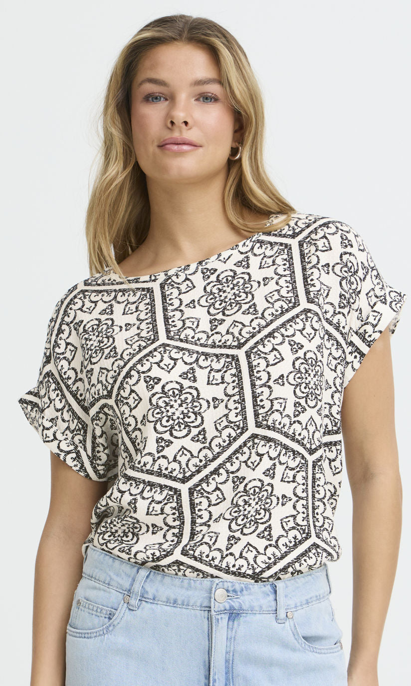 Woman wearing a black and white patterned top with light blue jeans on a white background