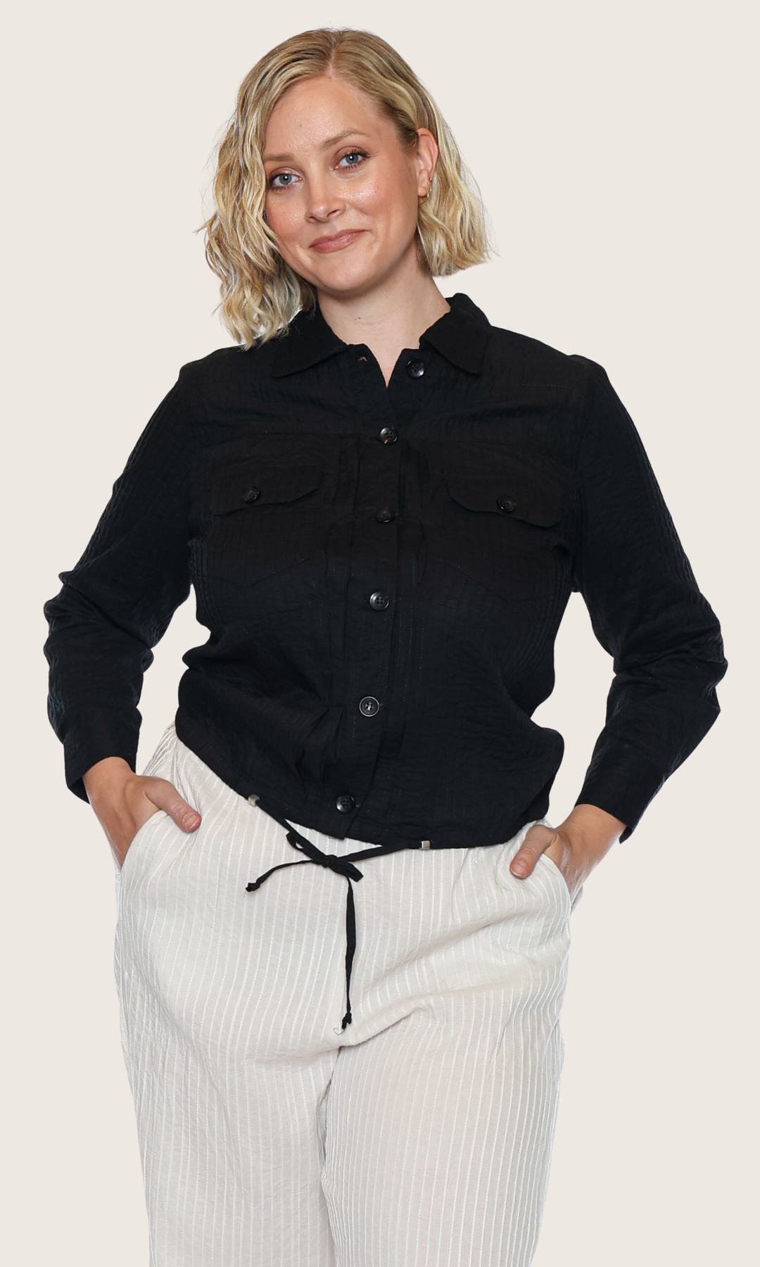 Woman wearing a black shirt and white pants on a plain background