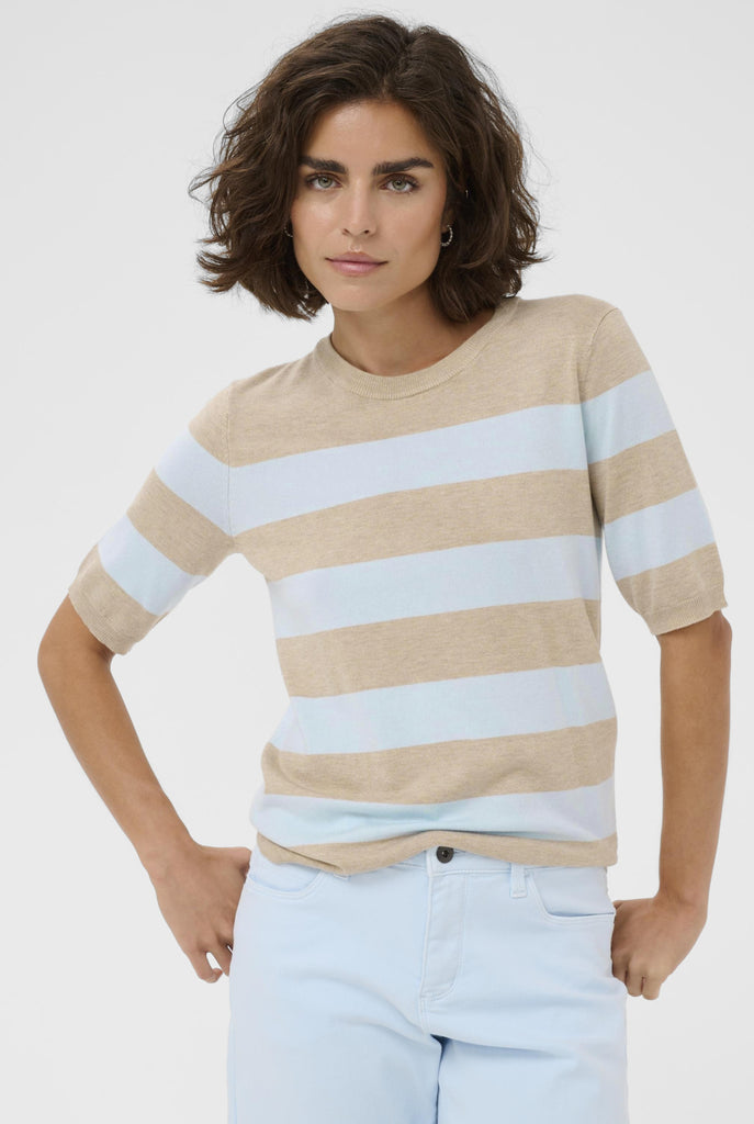 Woman wearing a beige and light blue striped sweater with light blue jeans on a white background
