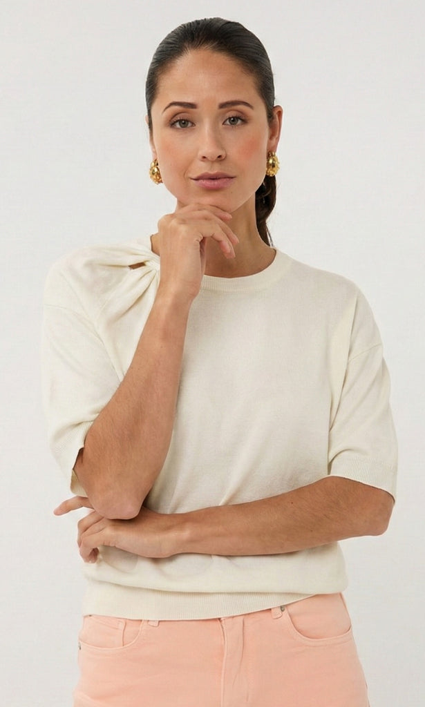 Woman wearing a cream sweater and pink pants against a white background