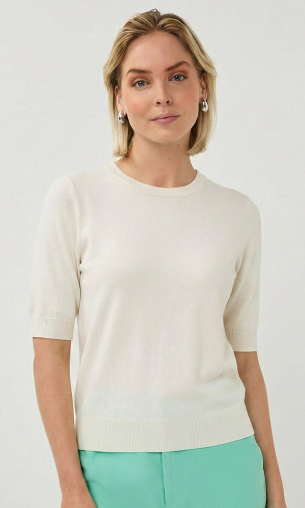 Woman wearing a cream sweater and green pants against a white background