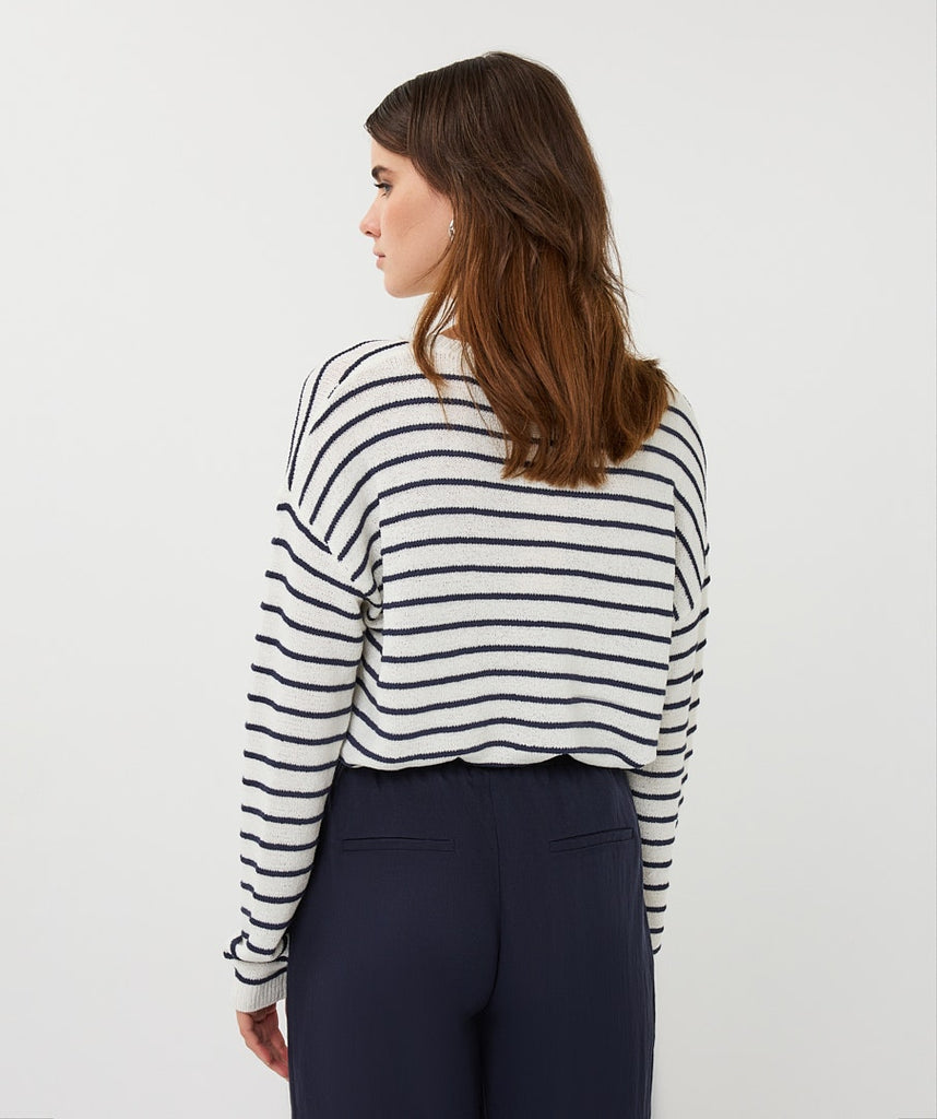 Woman wearing a black and white striped sweater and navy pants on a white background