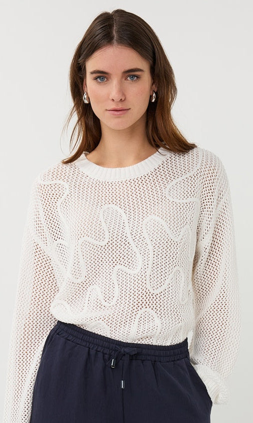Woman wearing a white knit top with a subtle pattern on a plain background