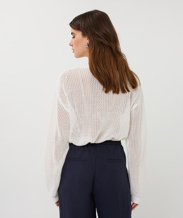 Woman wearing a white textured blouse and navy pants on a light gray background