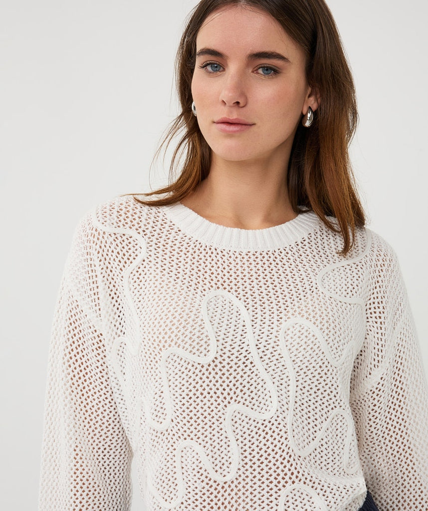 Woman wearing a white knit sweater against a plain background