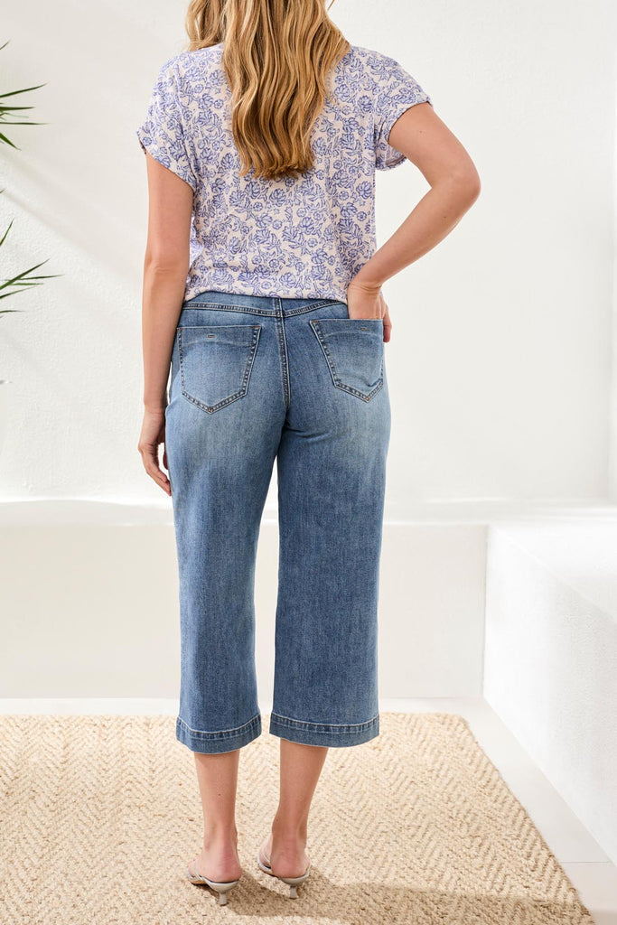 Woman wearing a floral top and blue jeans standing in a minimal indoor setting.
