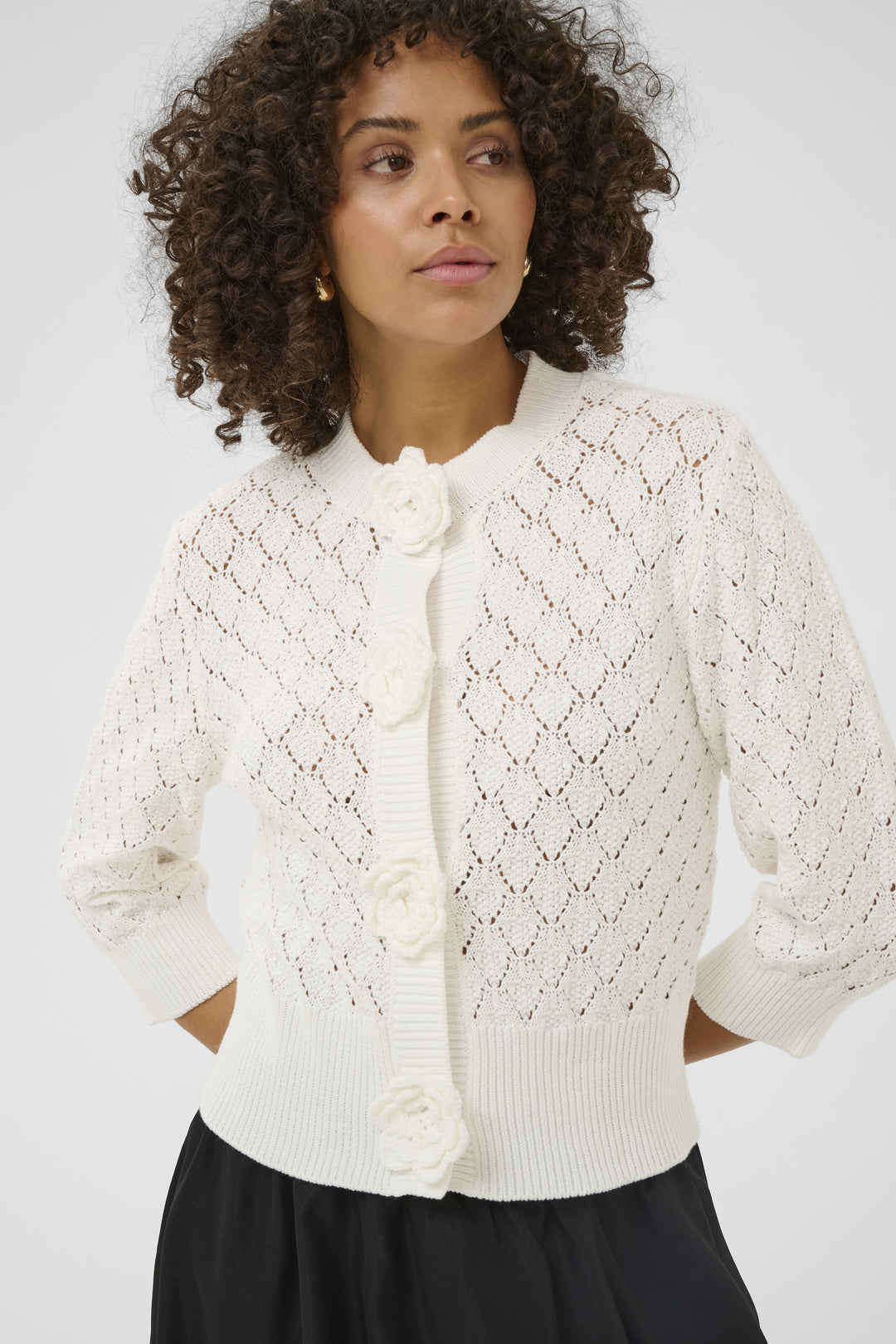 Woman wearing a white textured cardigan against a plain background