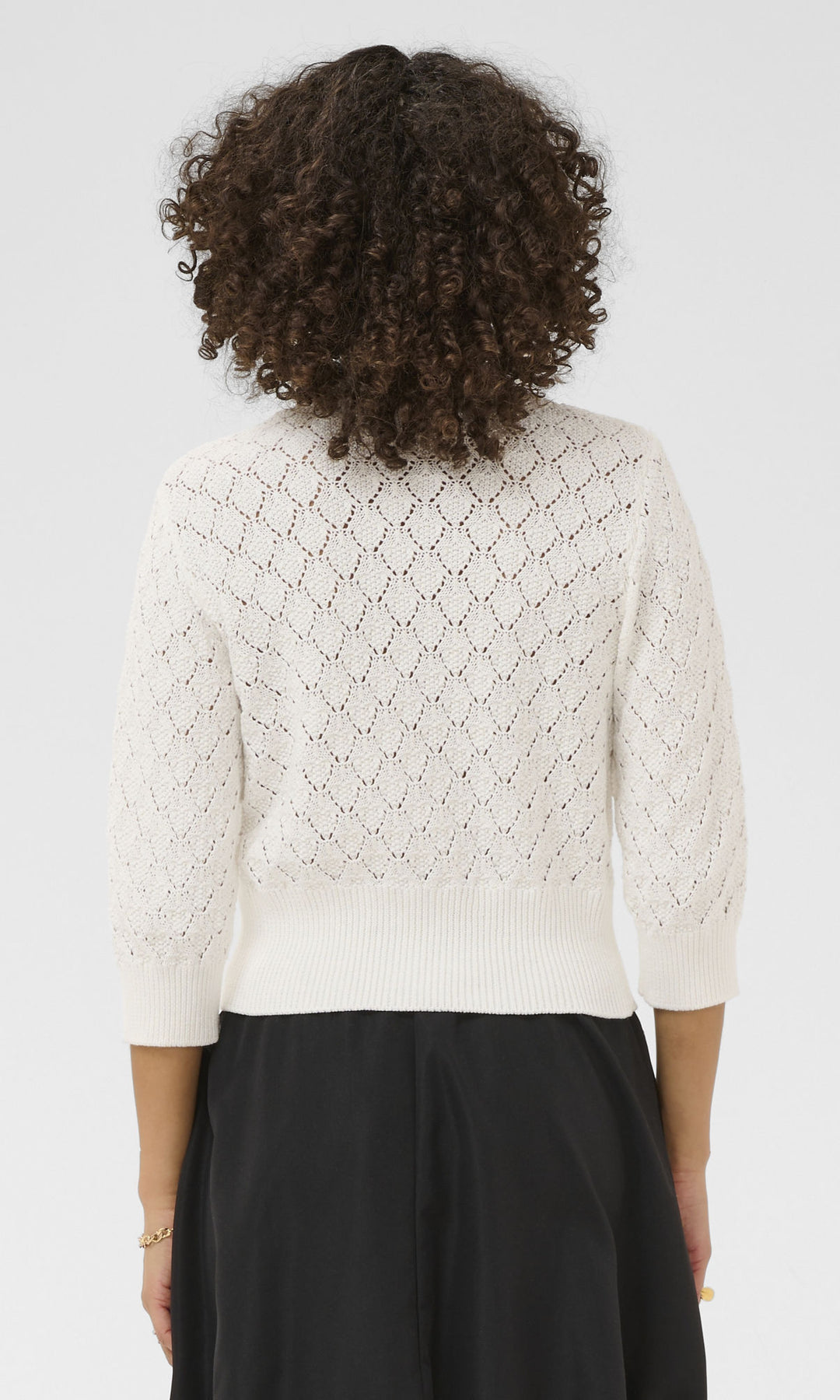 Person wearing a white textured sweater and black skirt on a light gray background