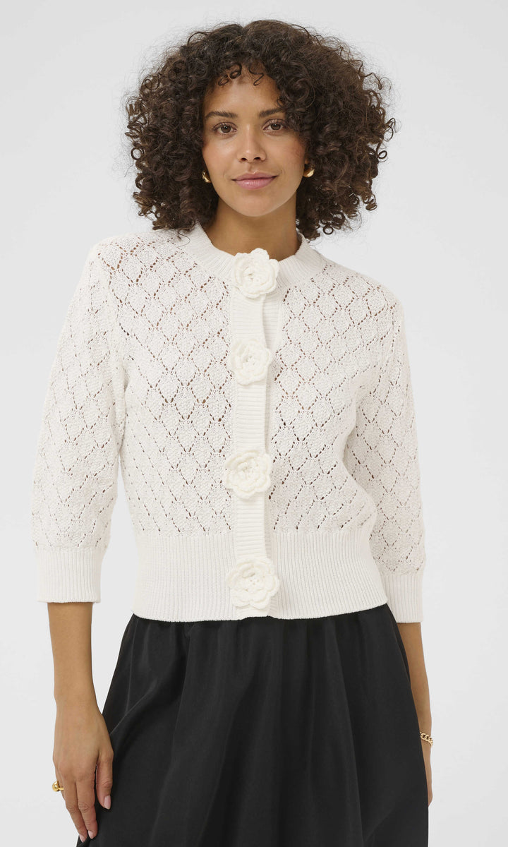 Woman wearing a white lace jacket with floral details on a plain background