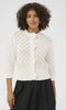 Woman wearing a white lace jacket with floral details on a plain background