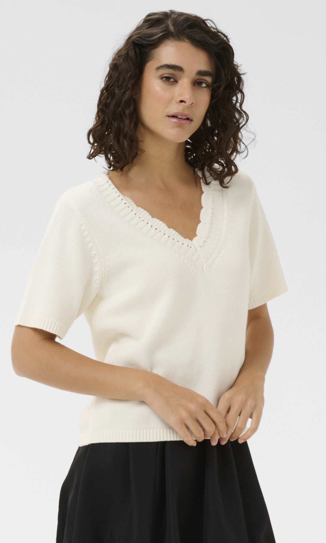 Woman wearing a white sweater with a V-neck and short sleeves on a plain background