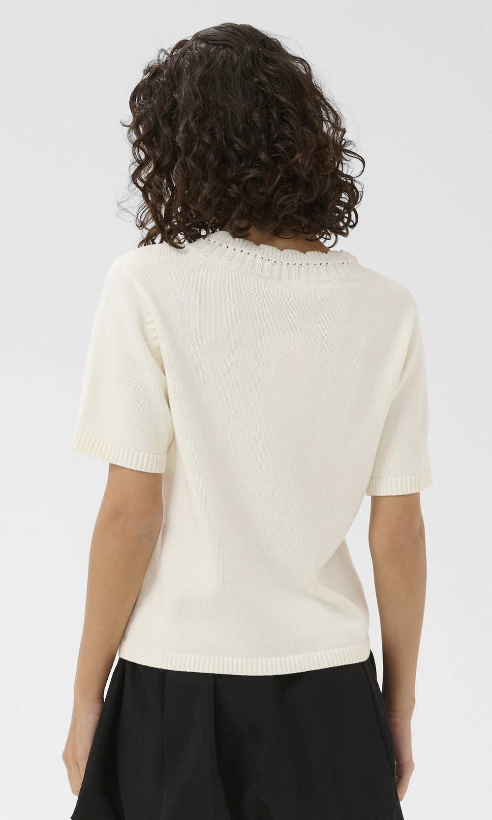 Back view of a person wearing a cream-colored short-sleeve top on a white background