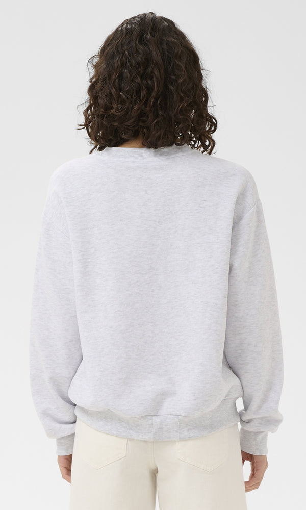 Person wearing a light gray sweater and white pants on a plain background