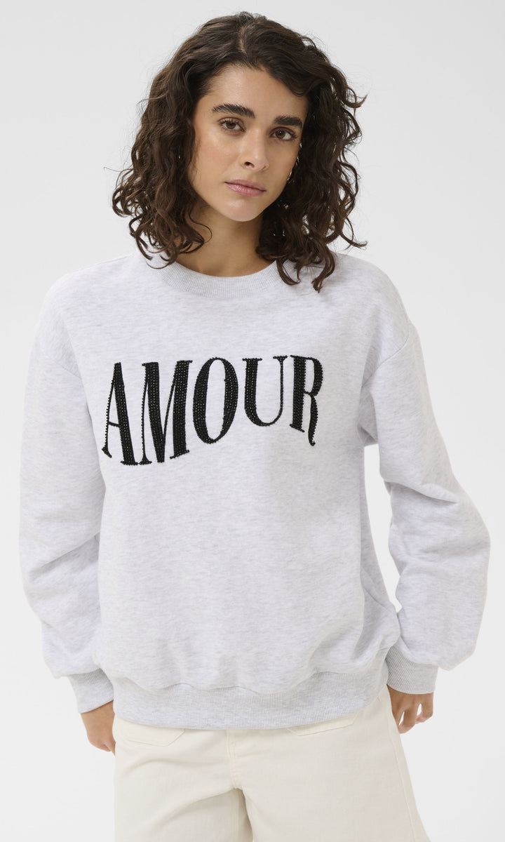 Person wearing a gray sweatshirt with 'AMOUR' printed on it against a white background