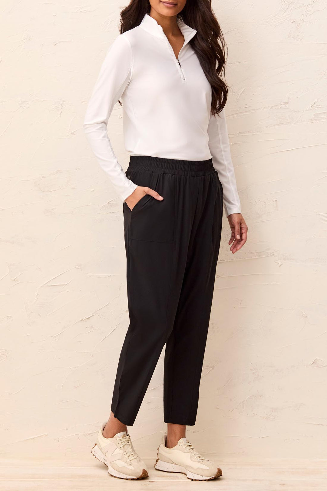 Woman wearing a white long-sleeve top and black pants against a light background