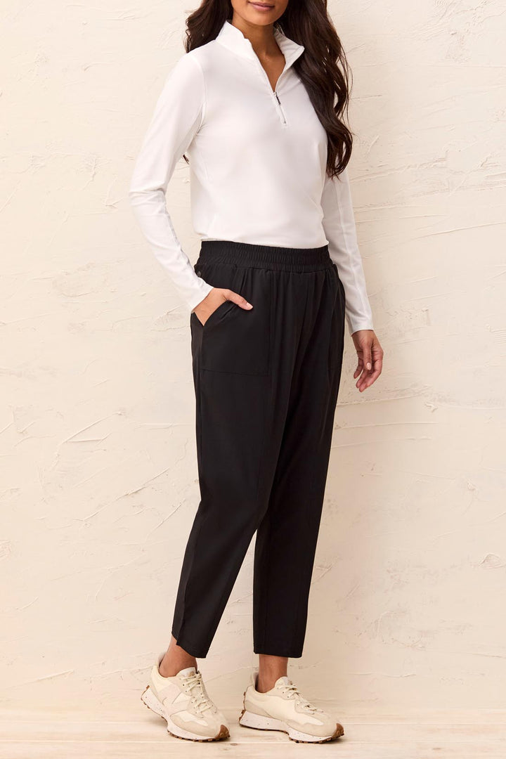 Woman wearing a white long-sleeve top and black pants against a light background