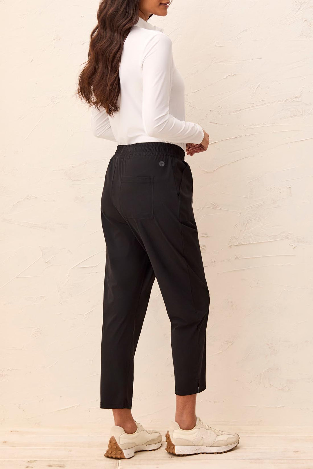 Person wearing a white blouse and black pants against a beige wall.
