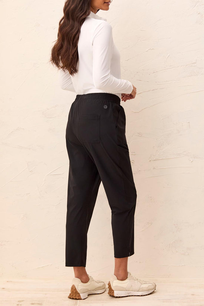 Person wearing a white blouse and black pants against a beige wall.