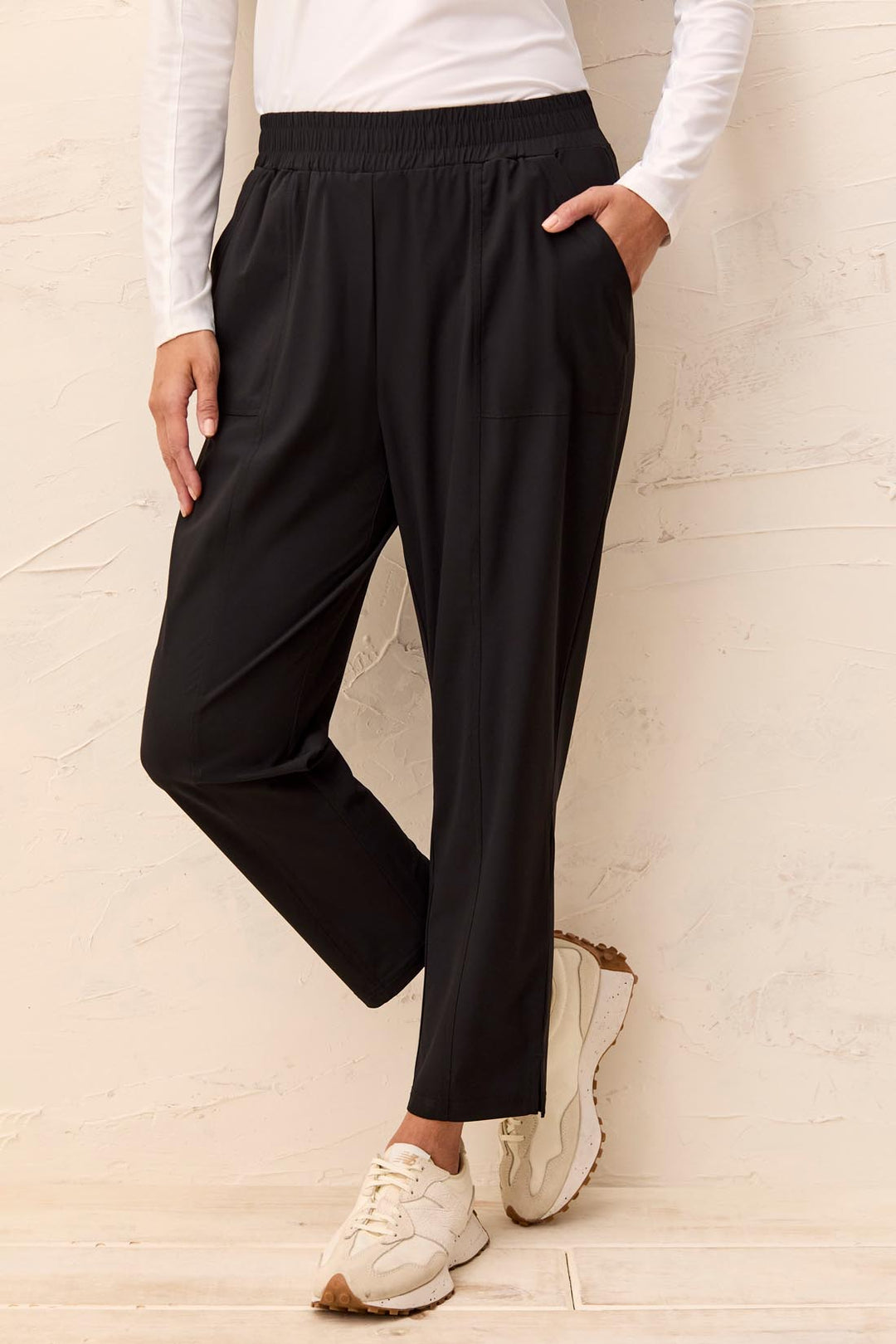 Person wearing black wide-leg pants and white sneakers against a light background
