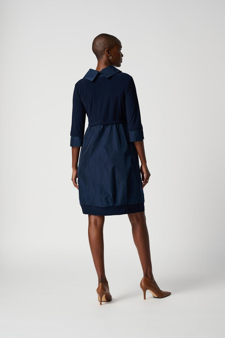 The back of a knee-length navy dress with a mock neckline, long cuffed sleeves, and front pockets.