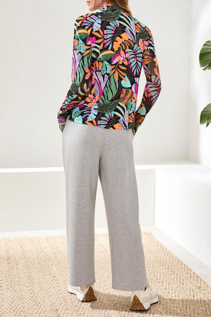 Person wearing a colorful floral blouse and gray pants in a minimal indoor setting.
