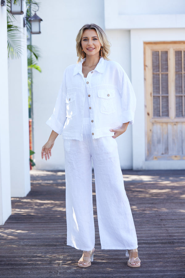 Woman wearing a white outfit standing on a wooden deck with a white building in the background.