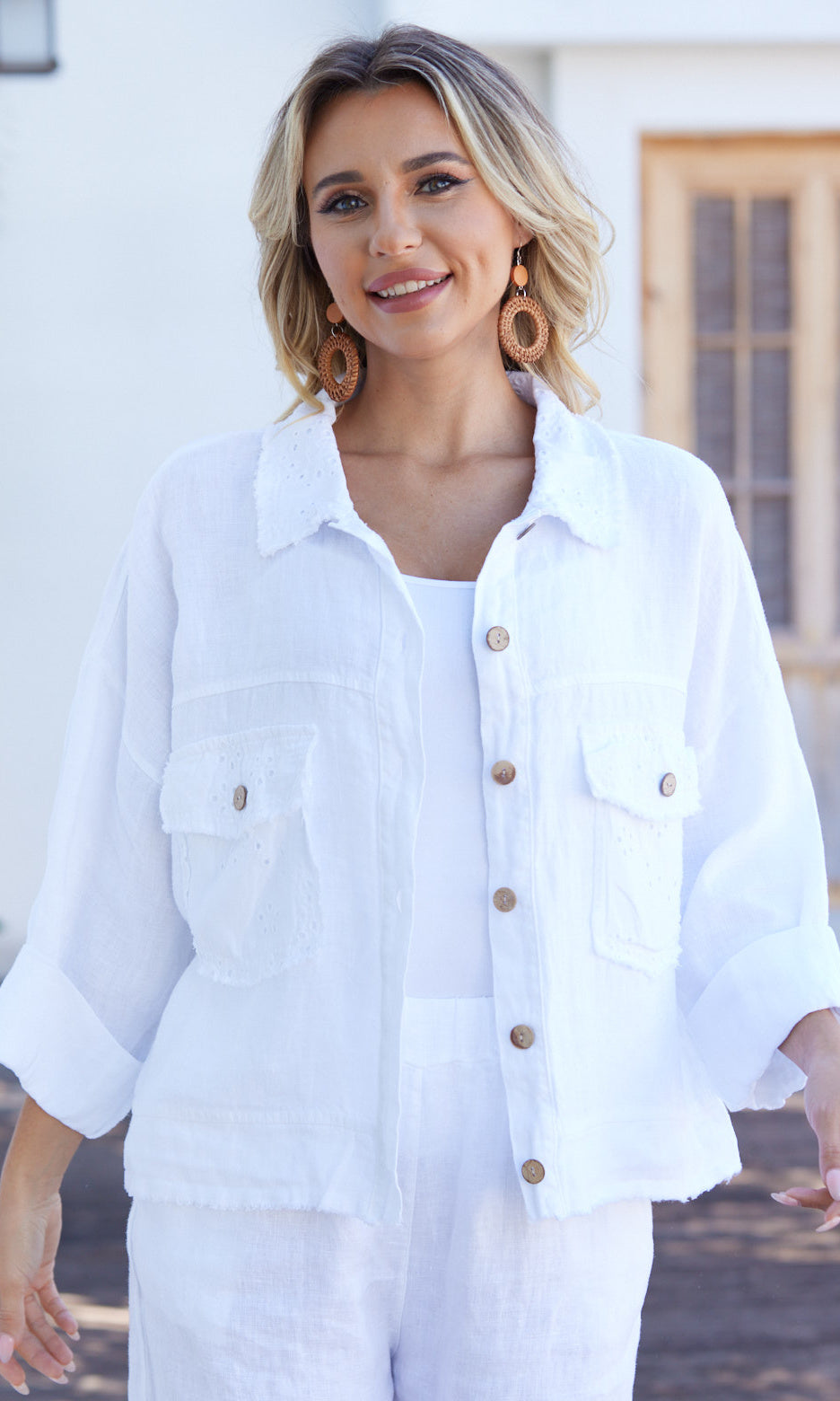 Woman wearing a white denim jacket with wooden buttons outdoors.