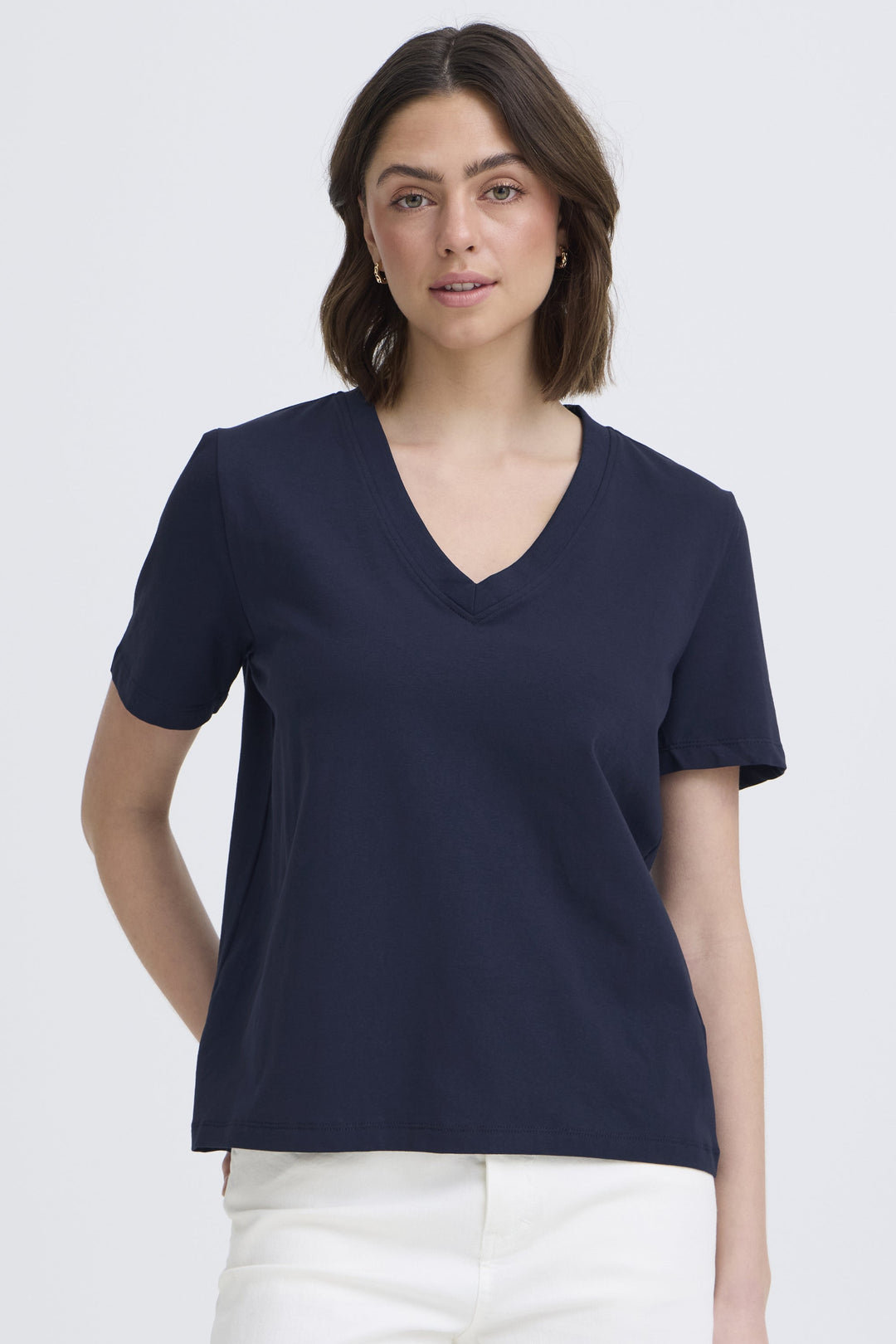 Woman wearing a navy blue V-neck t-shirt and white pants on a light gray background