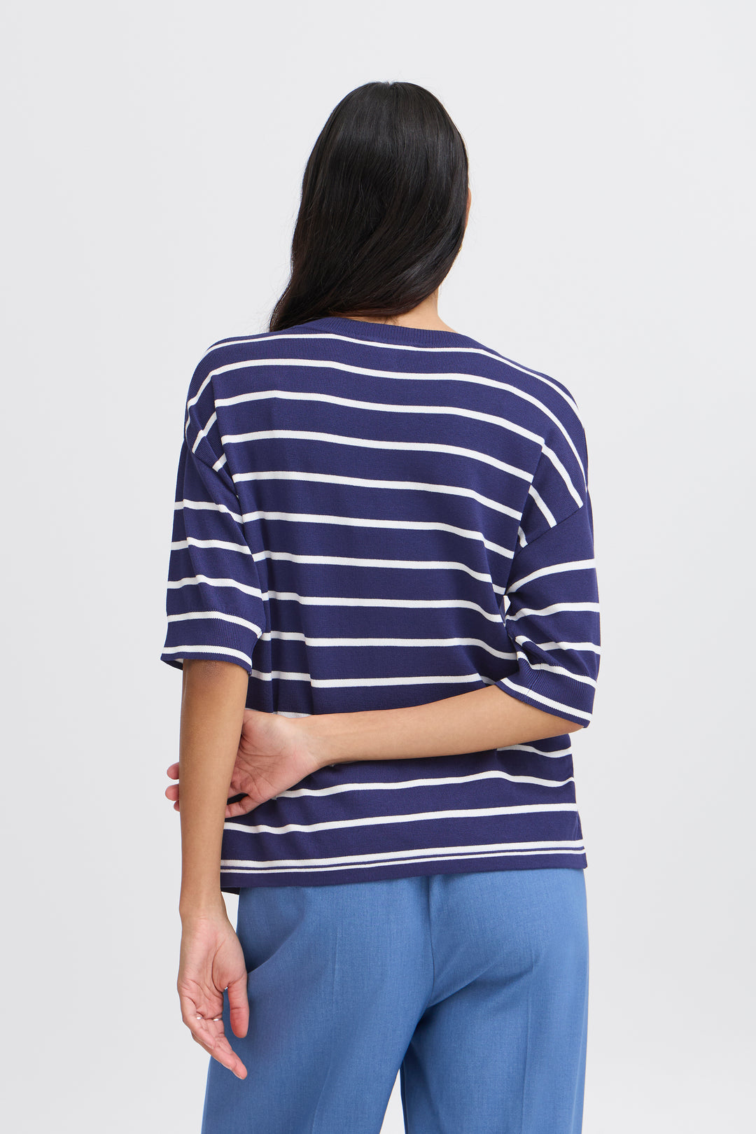 Person wearing a navy and white striped shirt with blue pants on a light gray background