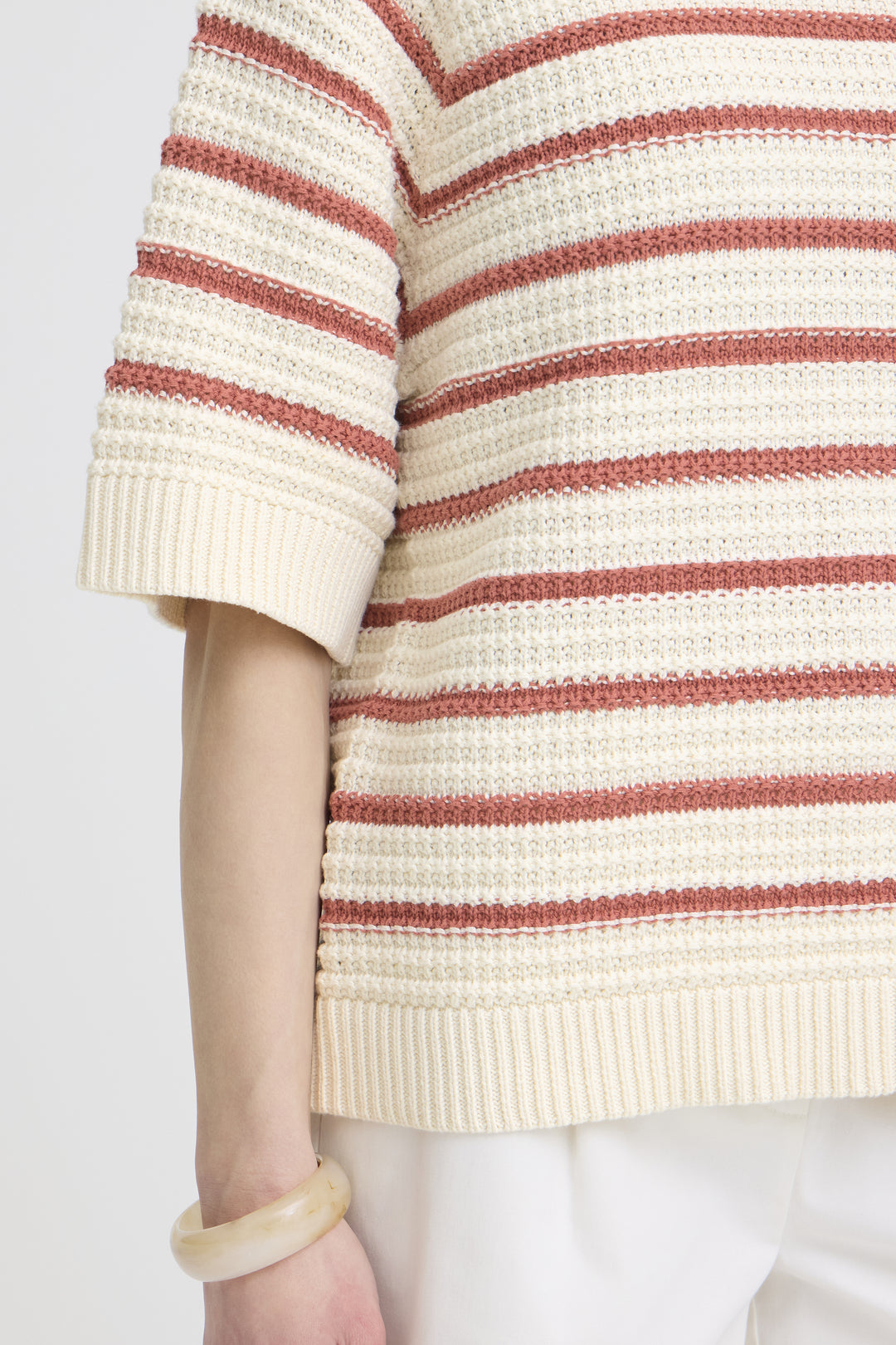 Close-up of a person wearing a striped sweater with red and beige colors on a plain background.