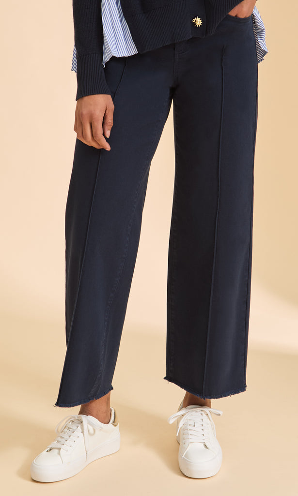 Navy pants worn with a white shirt and white sneakers on a beige background