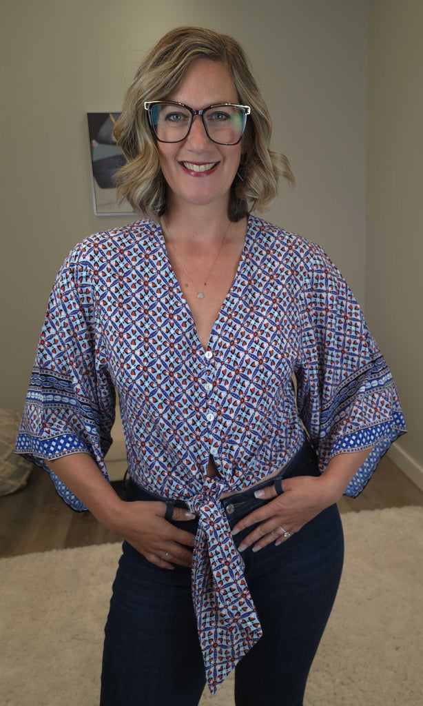 Woman wearing a patterned blouse and dark pants indoors.