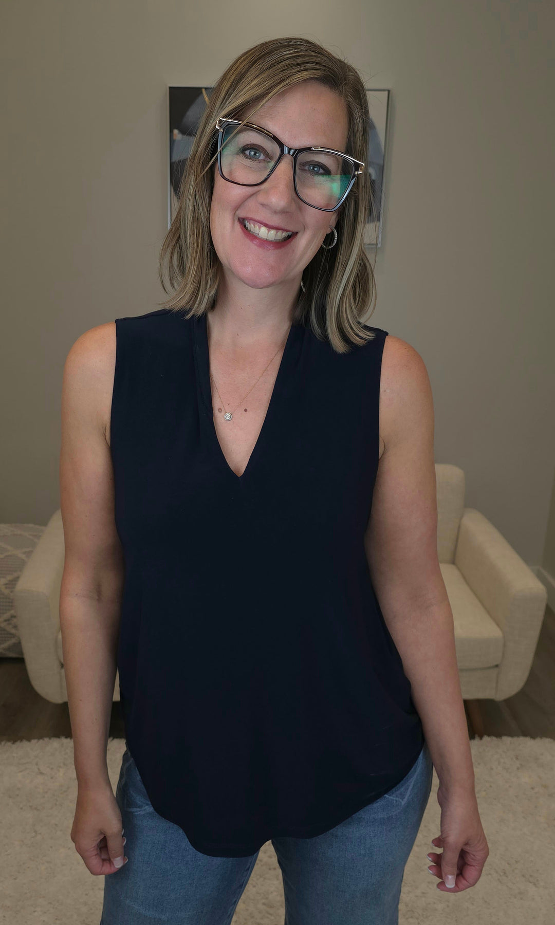Woman wearing a black sleeveless top and blue jeans indoors.