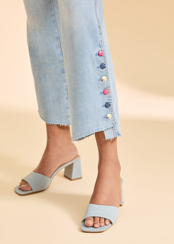 Light blue sandals worn with light blue jeans featuring colorful buttons on a beige background