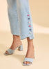 Light blue sandals worn with light blue jeans featuring colorful buttons on a beige background