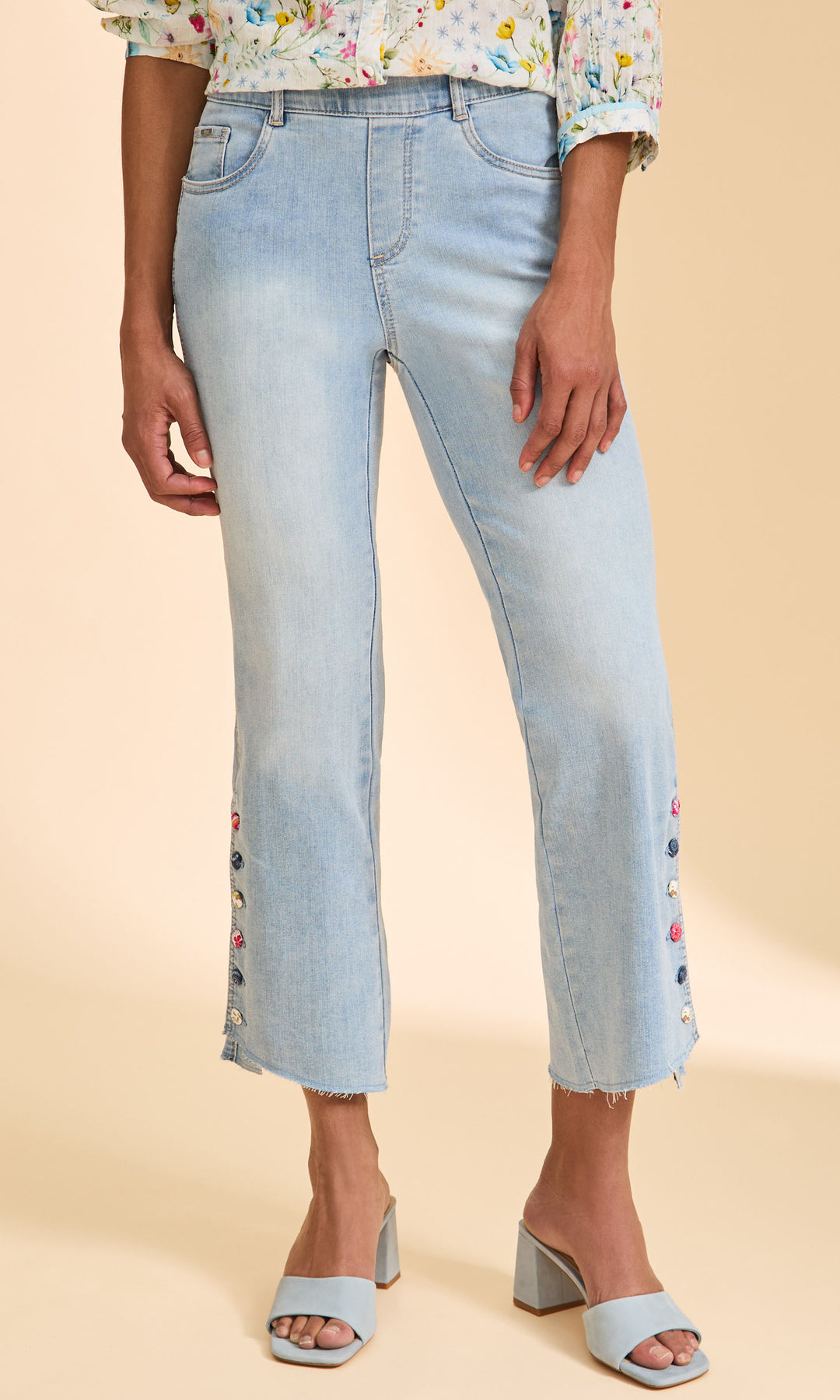 Person wearing light blue jeans with floral embroidery on a beige background