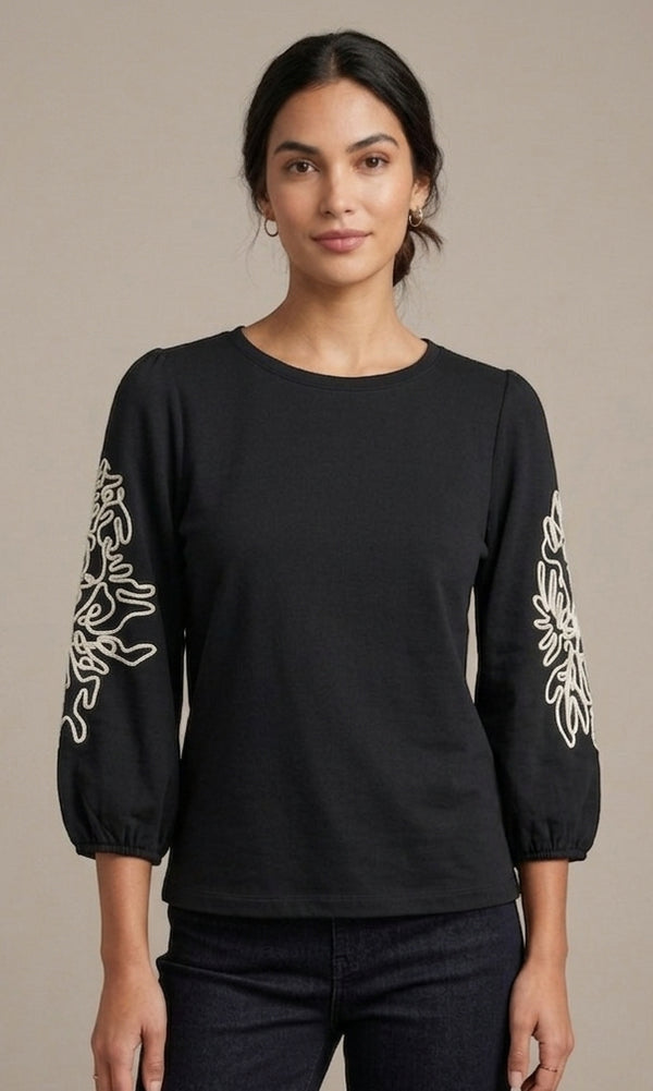 Woman wearing a black long-sleeve top with white floral patterns on a beige background