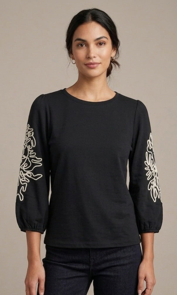 Woman wearing a black long-sleeve top with white floral patterns on a beige background