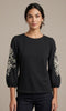 Woman wearing a black long-sleeve top with white floral patterns on a beige background