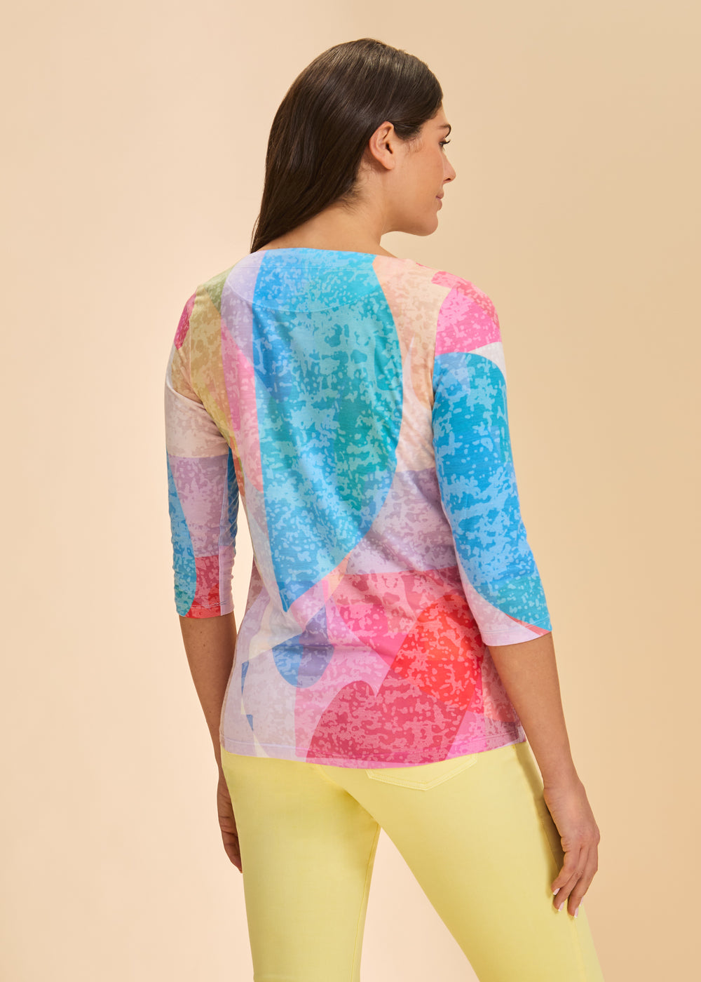 Woman wearing a colorful tie-dye top and yellow pants on a beige background