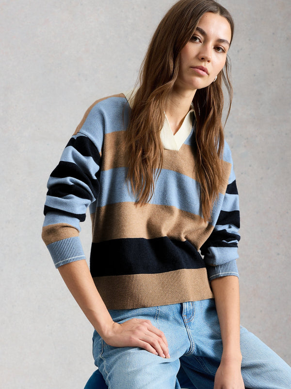 Woman wearing a striped sweater and jeans sitting on a blue chair against a gray background