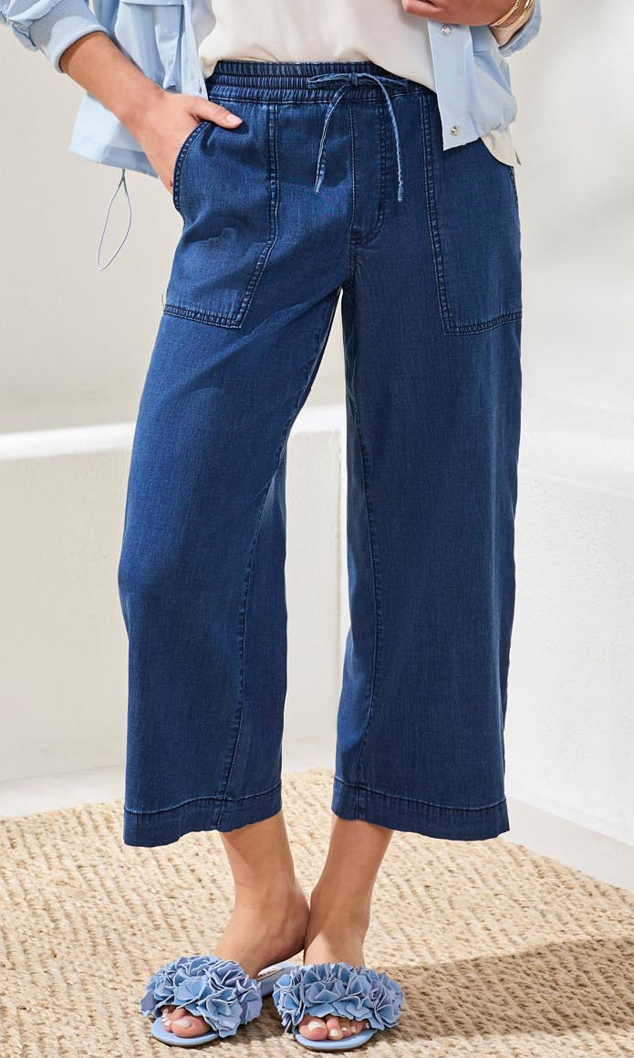 Person wearing blue wide-leg jeans and matching sandals on a neutral background