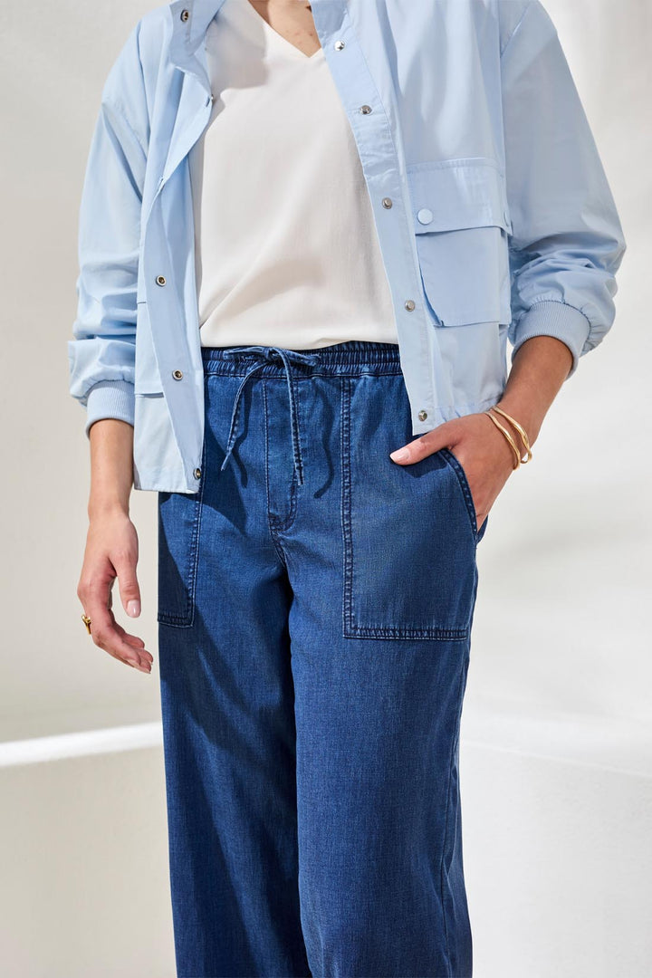 Person wearing a light blue shirt, white top, and blue jeans on a plain background