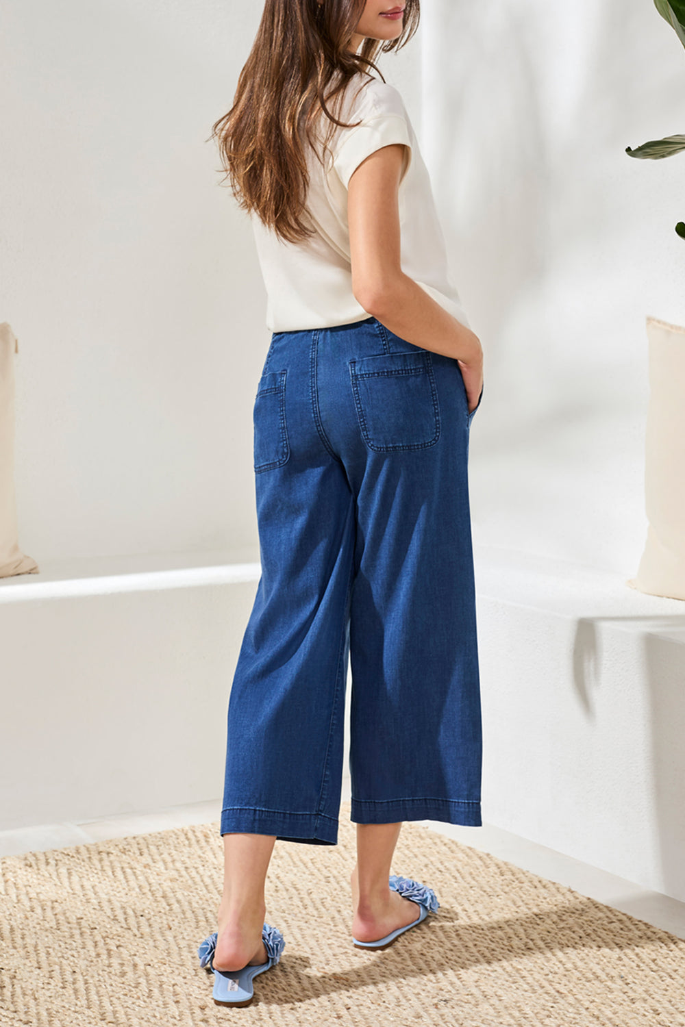 Woman wearing blue wide-leg pants and a white top in a minimal indoor setting.