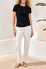 Woman wearing a black t-shirt and white pants standing in a minimalistic room.