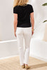 Woman wearing a black t-shirt and white pants standing in a room with a neutral color scheme.