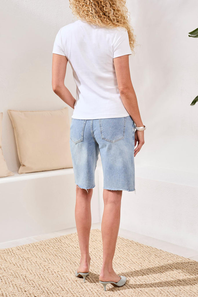 Woman wearing a white t-shirt and light blue denim shorts in a minimal indoor setting.