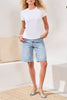 Woman wearing a white t-shirt and light blue denim shorts in a minimal indoor setting.