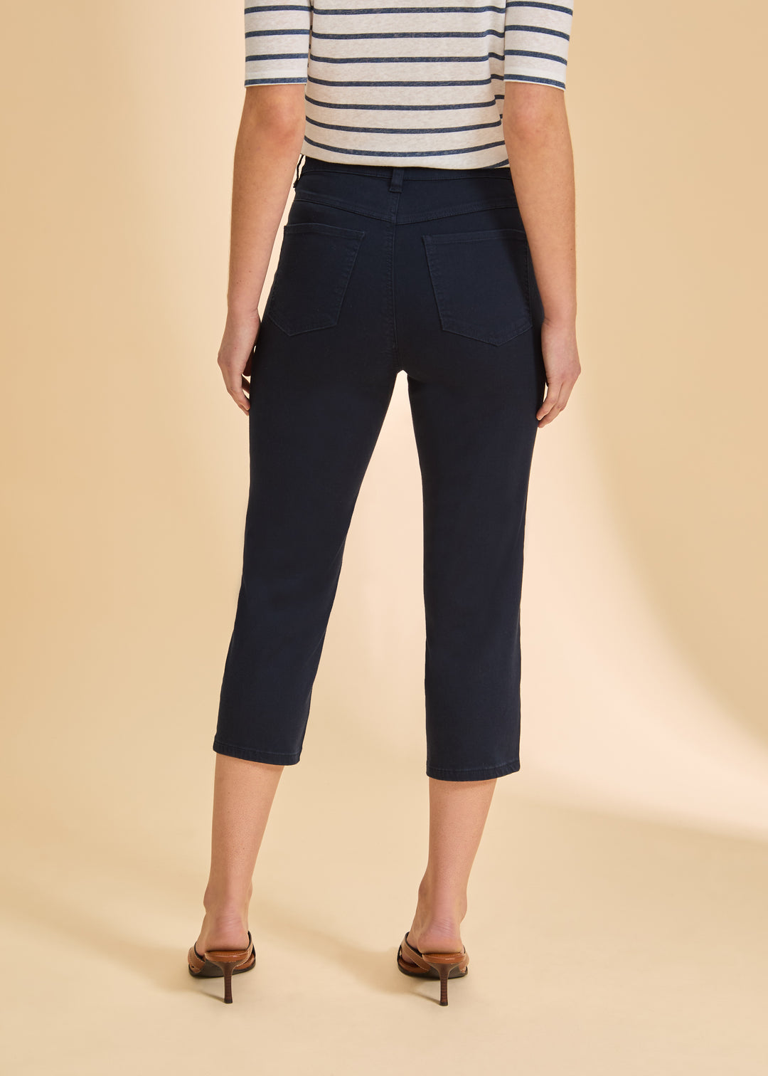 Person wearing navy capri pants and a striped shirt on a beige background