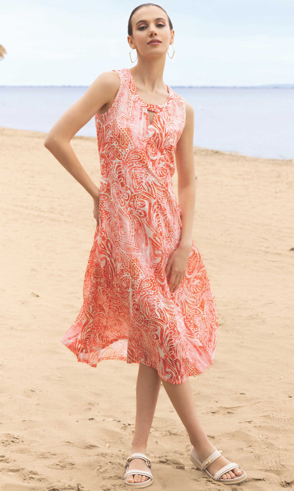 Woman in a patterned dress standing on sand with ocean in the background